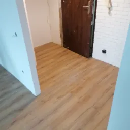 Układanie paneli podłogowych w trakcie remontu mieszkania, widoczne niedokończone ściany i wystające kable.