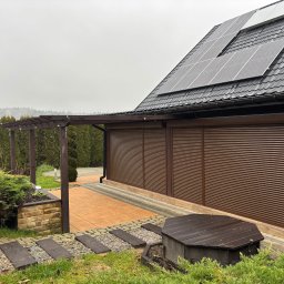 Letyro Bartosz Lekki - Brązowe, poziome panele osłonowe zamknięte na budynku z panelami słonecznymi na dachu, widok z ogrodu z pergolą i ścieżką.