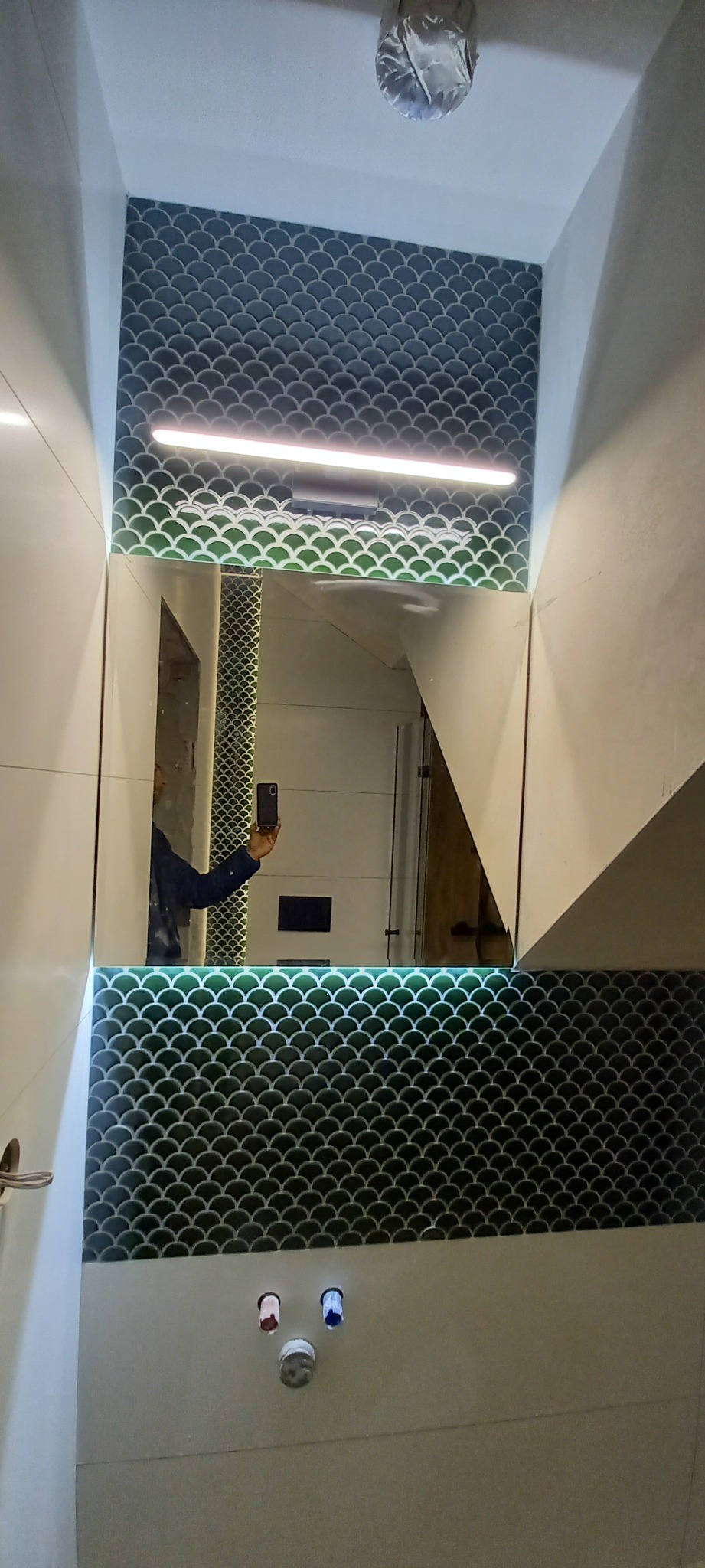 Wykończona łazienka z lustrem podświetlanym LED i dekoracyjnymi płytkami w kształcie rybiej łuski, widoczne przyłącza wodne z zaślepkami.