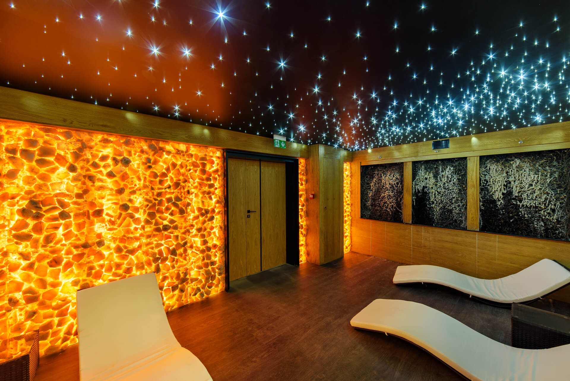 Nowoczesne wnętrze relaksacyjne z podświetlaną ścianą z kamienia solnego, sufitem imitującym rozgwieżdżone niebo i leżankami.