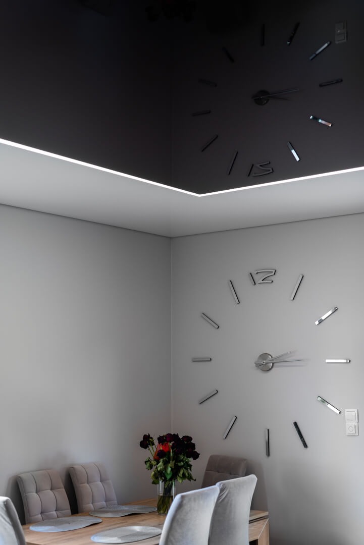 Czarne lustrzane wykończenie sufitu z podświetleniem LED i dekoracyjnym zegarem ściennym w nowoczesnym wnętrzu.