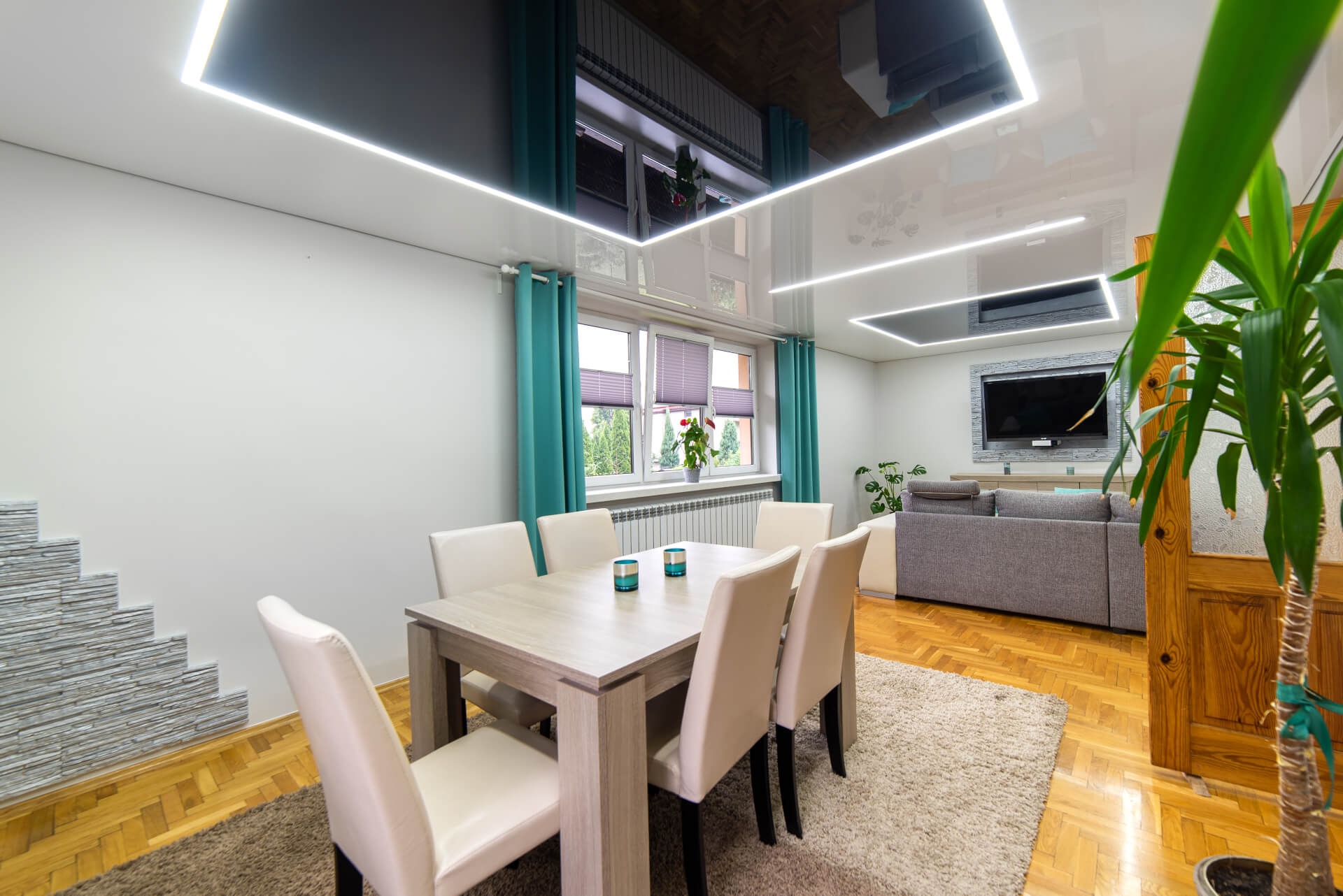 Jasne wnętrze jadalni z błyszczącym sufitem z liniowym oświetleniem LED, szare krzesła i stół, dekoracyjna ściana z kamienia imitującego schody.