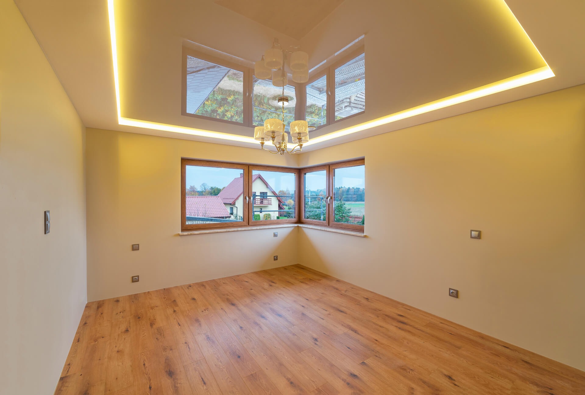 Jasny pokój po remoncie z drewnianą podłogą, narożnym oknem z widokiem na dom i ogórd, sufitem napinanym z odbiciem i oświetleniem LED.