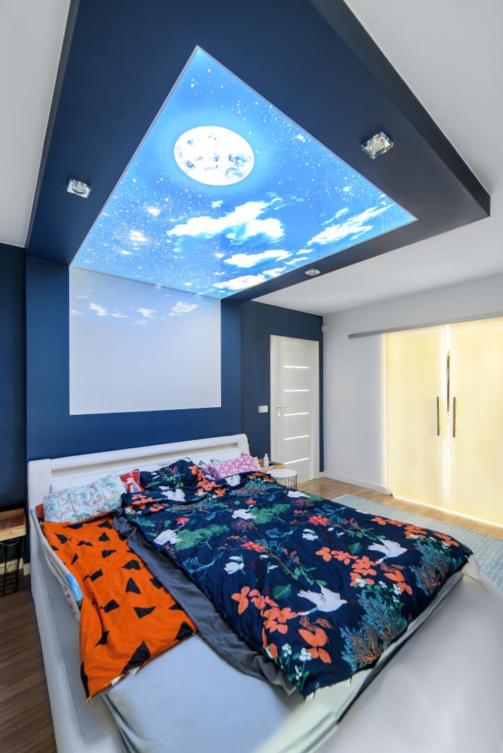 Sypialnia z podświetlanym sufitem z motywem księżyca i chmur, ciemnoniebieskie ściany, białe drzwi i przesuwne drzwi z mlecznego szkła.
