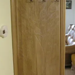 Drewniana zabudowa drzwiowa z rzeźbionym motywem pawia i metalowymi haczykami na ubrania, widoczna w korytarzu mieszkania.