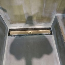 Profis - Przygotowanie podłoża w kabinie prysznicowej z zamontowanym odpływem liniowym, ściany i podłoga pokryte warstwą wyrównującą.