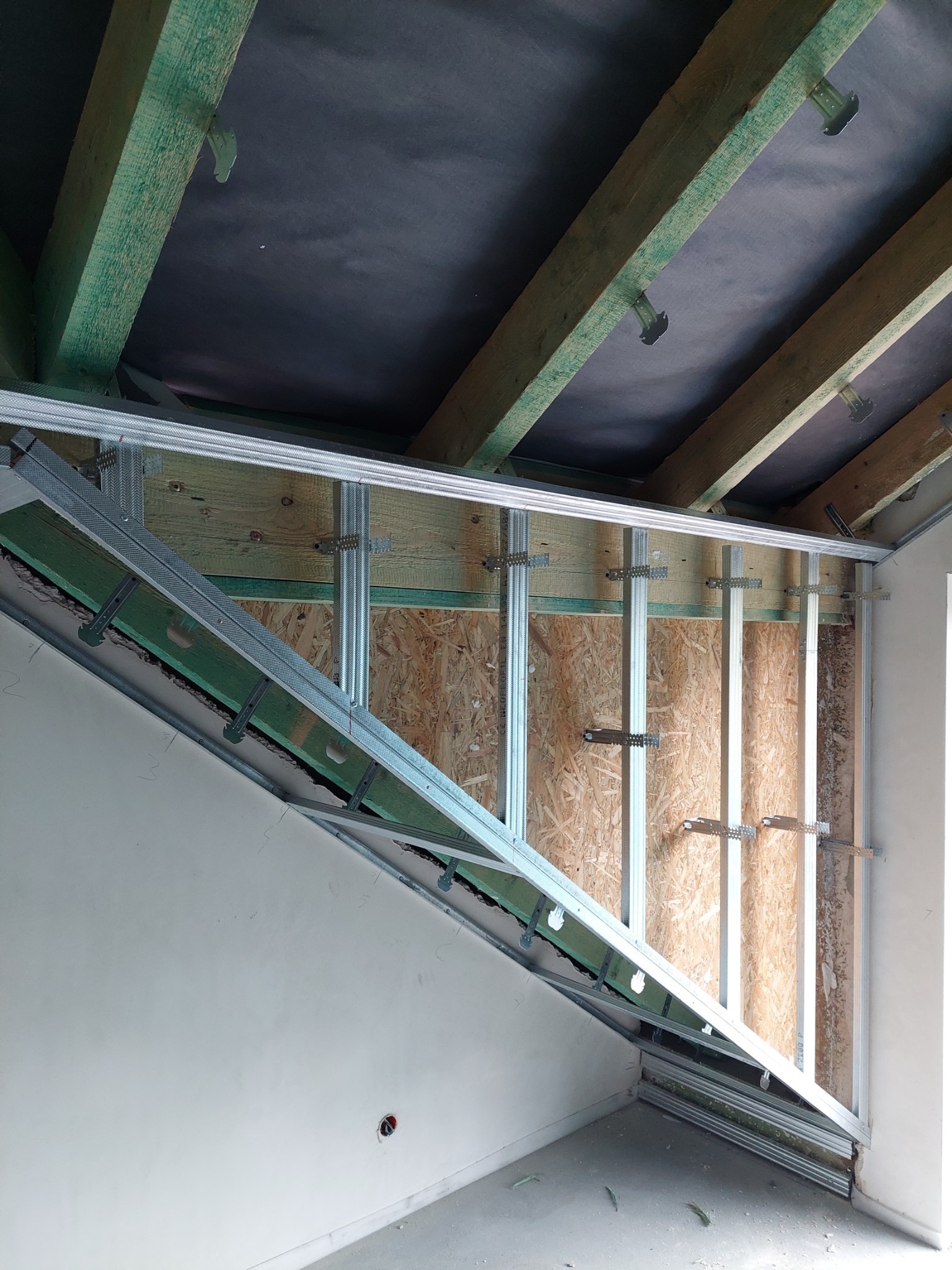 Szkielet konstrukcji z profili metalowych pod zabudowę na poddaszu, widoczne drewniane elementy więźby dachowej i płyta OSB na ścianie szczytowej.