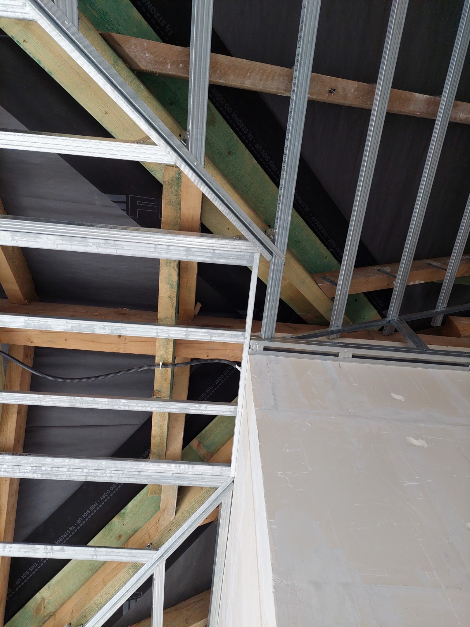 Konstrukcja sufitu podwieszanego z profili metalowych i drewnianych belek, częściowo zakryta płytą gipsowo-kartonową przed wykończeniem, widoczne kable elektryczne.