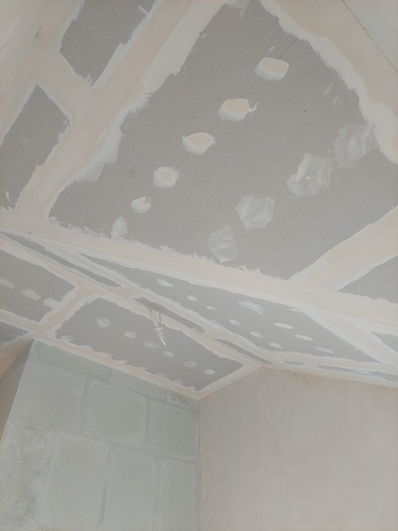 Sufit i górna część ściany w trakcie montażu płyt kartonowo-gipsowych, widoczne łączenia płyt zaszpachlowane, otwory po wkrętach również wypełnione szpachlą, surowe wykończenie.