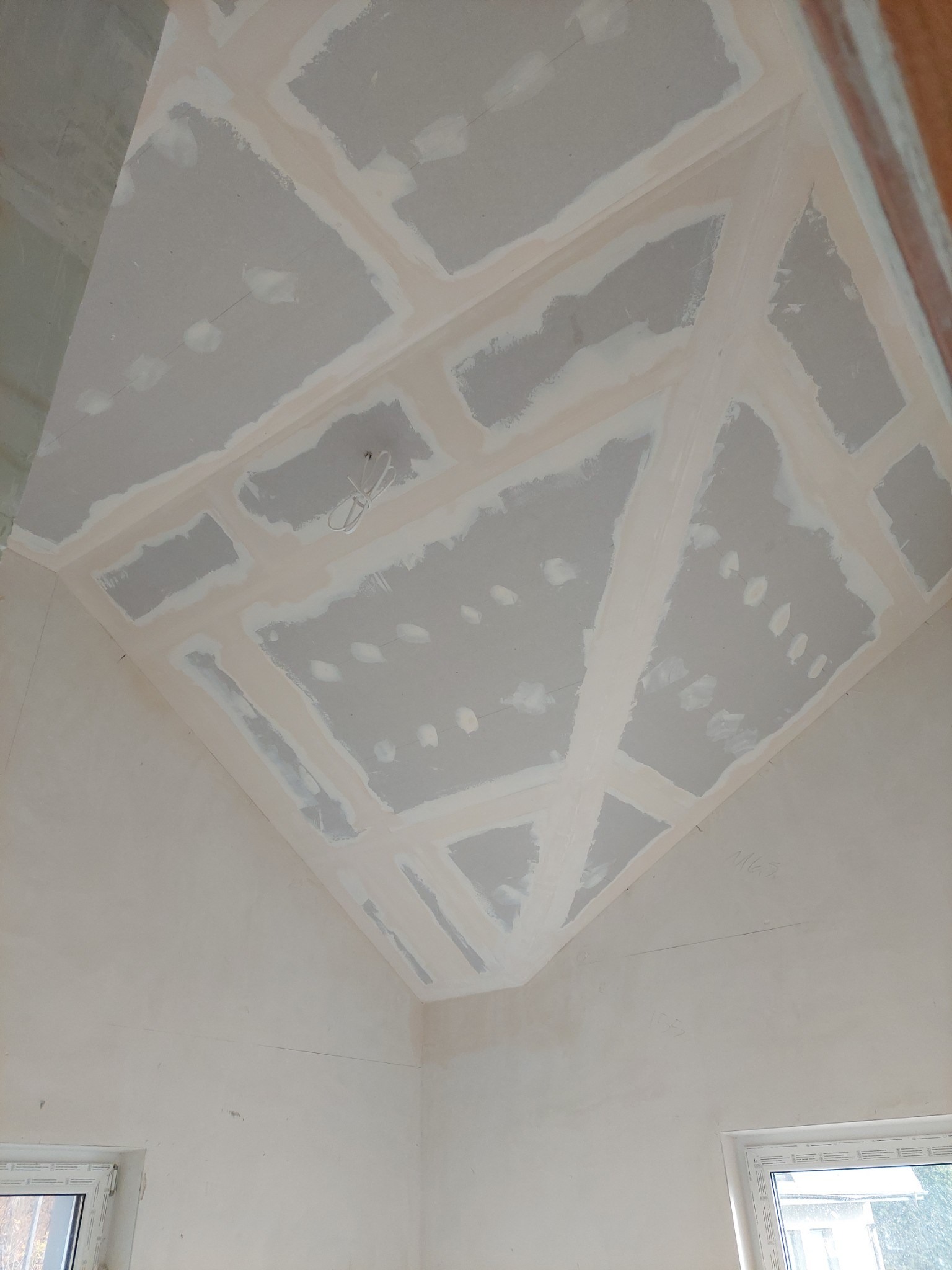 Skośny sufit poddasza z płyt kartonowo-gipsowych, szpachlowane łączenia widoczne pod światło, przygotowanie do dalszych prac wykończeniowych.