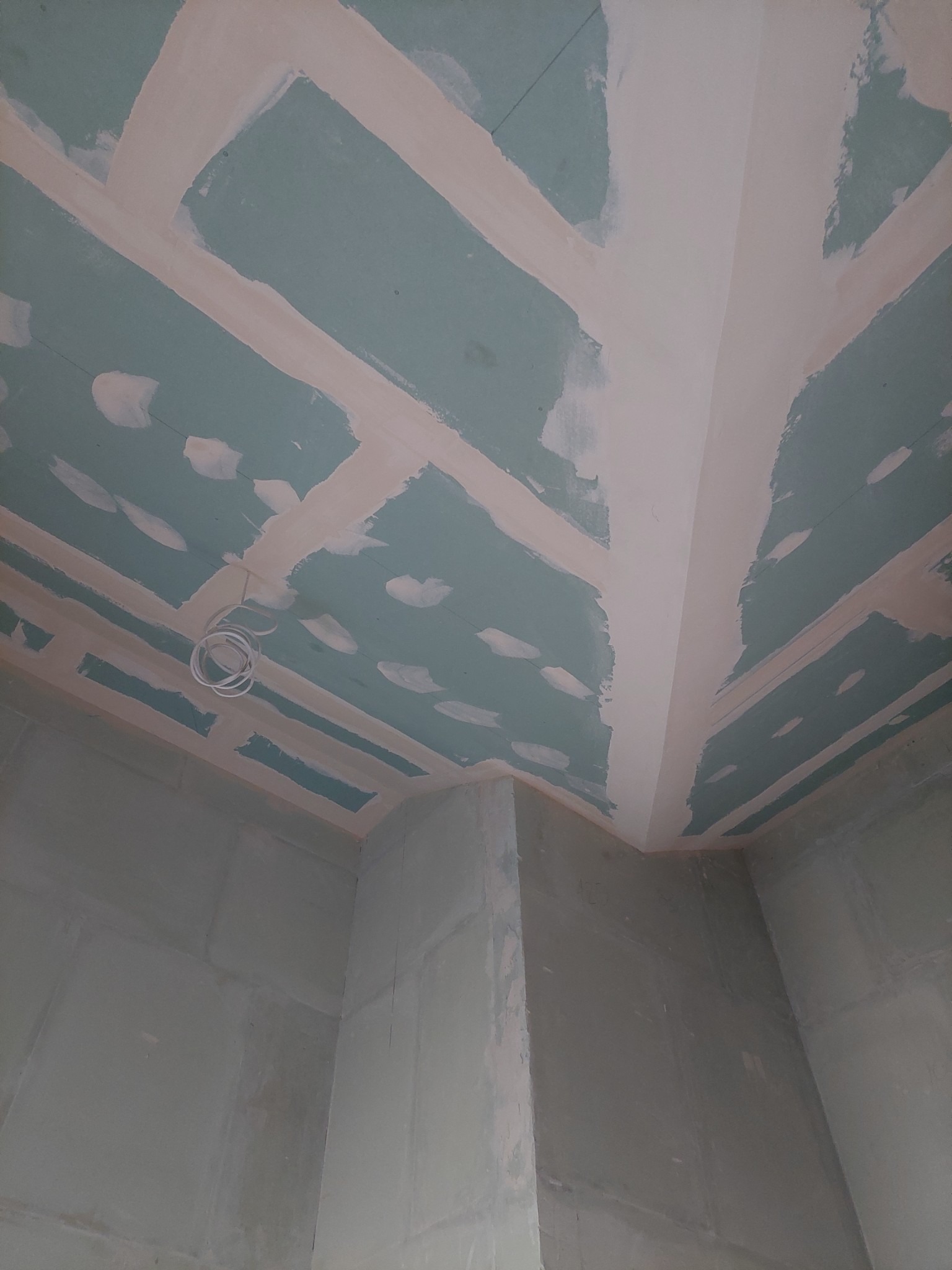 Nierówna powierzchnia sufitu z płyty gipsowo-kartonowej, wstępnie zagruntowana i z widocznymi łączeniami, z wiszącymi przewodami elektrycznymi.