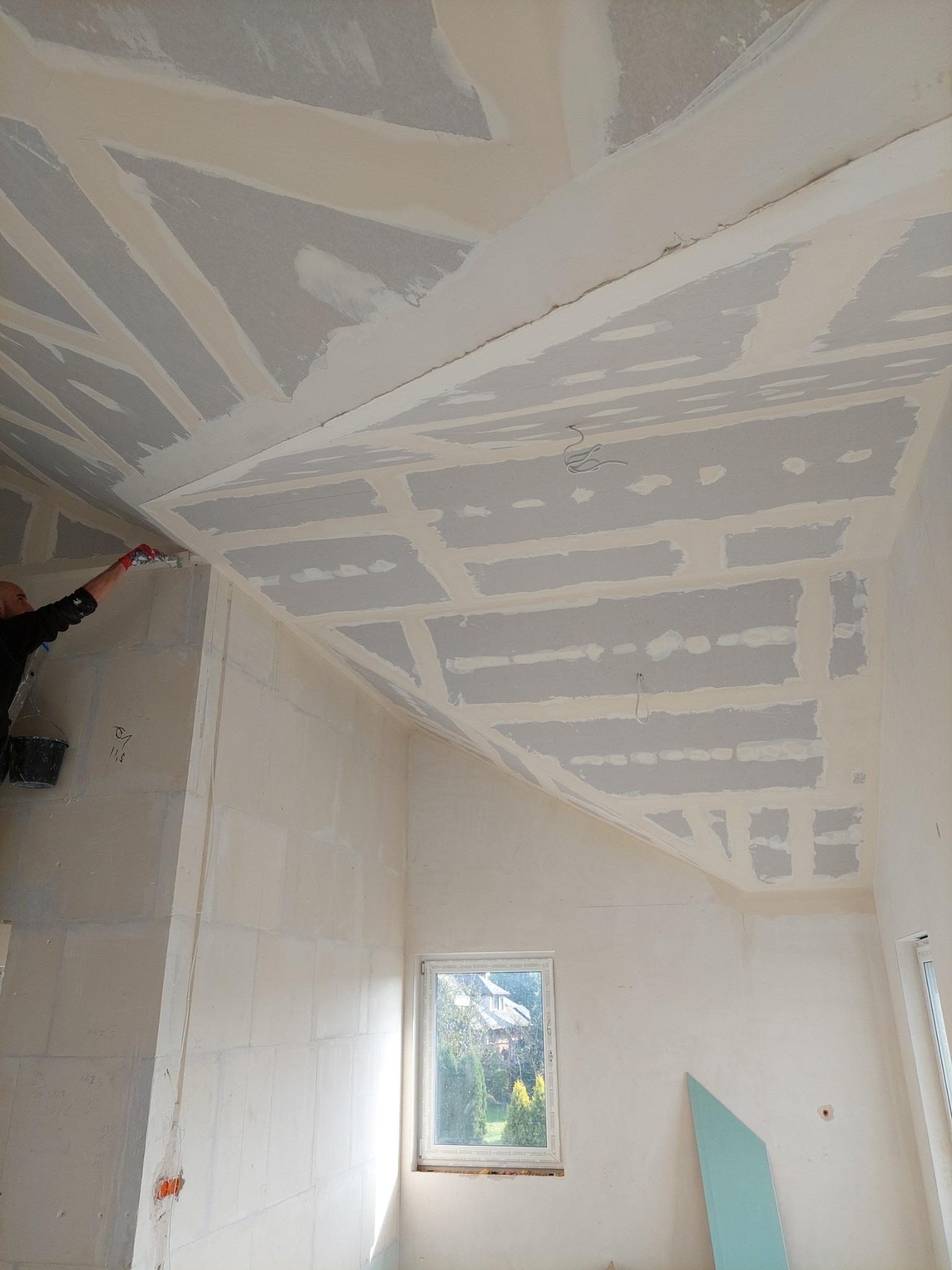 Montaż płyt karton gips na suficie poddasza, widoczne łączenia płyt i fragment pracującej osoby z narzędziem.