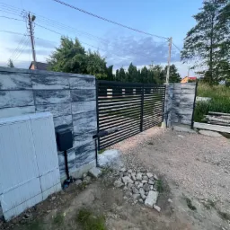 Automatyczna brama wjazdowa z szarych, wzorzystych bloczków w Krakowie, widoczny napęd i skrzynka sterująca.