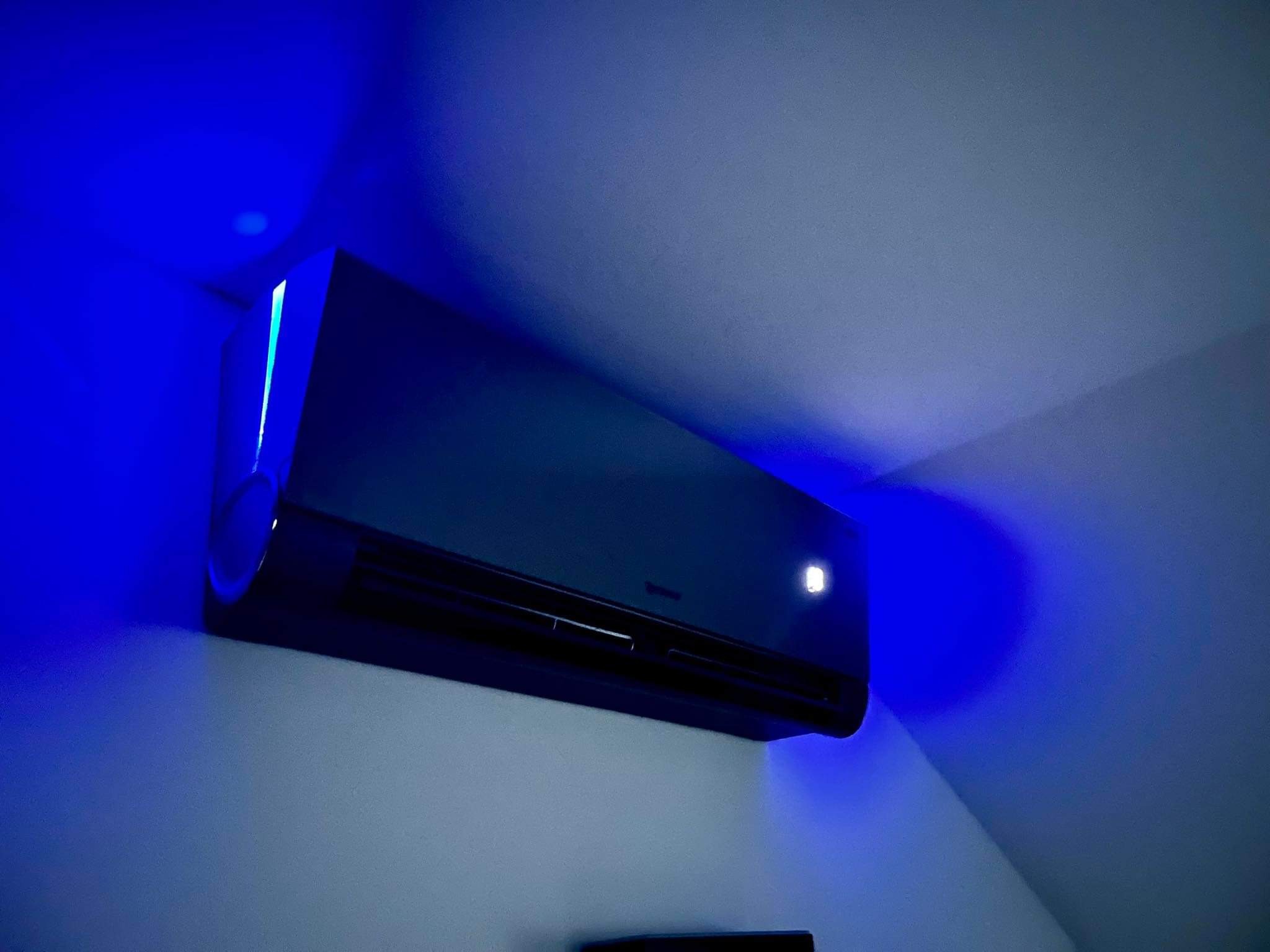 Czarny klimatyzator ścienny z podświetleniem LED w odcieniach niebieskiego, zamontowany w rogu pomieszczenia, widok z dołu.