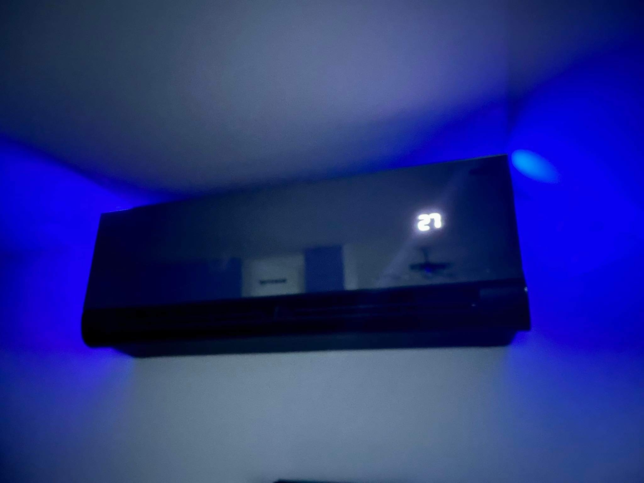 Czarny klimatyzator ścienny z wyświetlaczem temperatury 27 stopni, podświetlony niebieskim światłem.