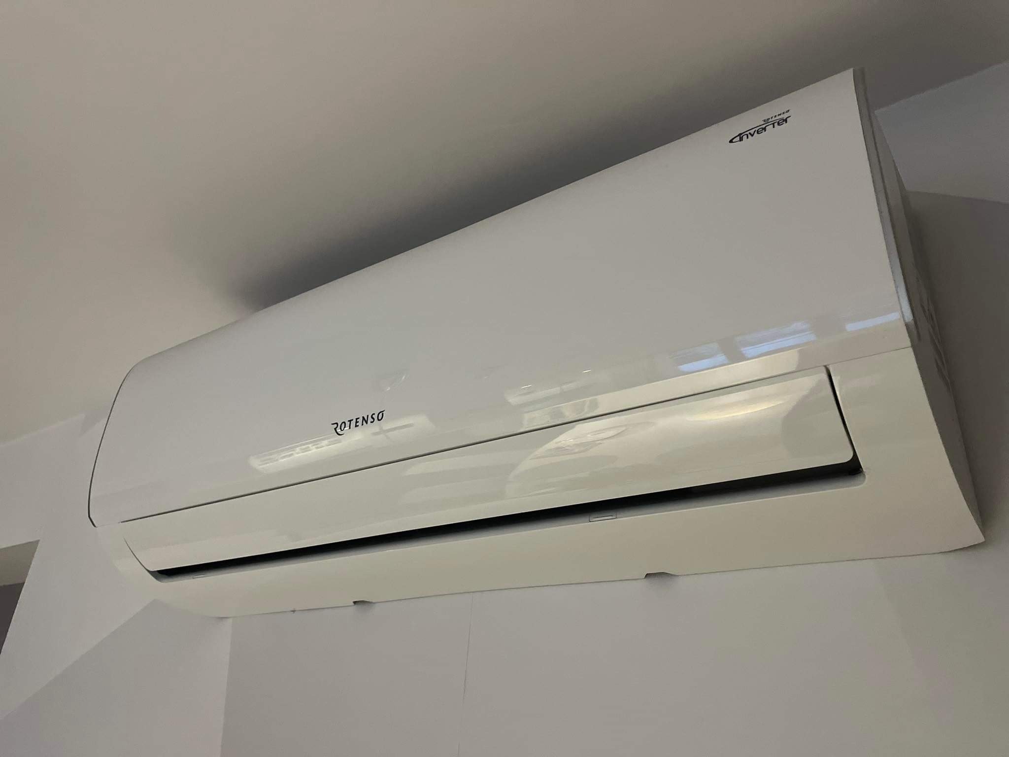 Biała jednostka wewnętrzna klimatyzacji Rotenso Inverter zamontowana na jasnej ścianie w rogu pomieszczenia, widoczne delikatne cienie na ścianie.