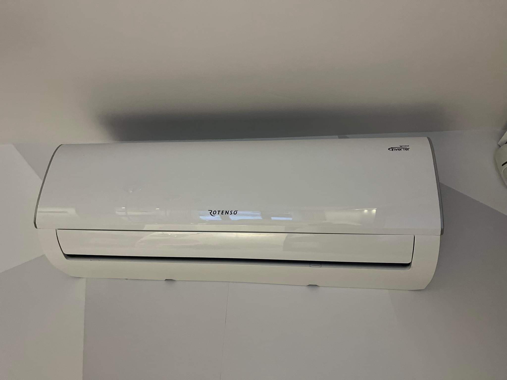 Biała klimatyzacja Rotenso typu split zamontowana na szarej ścianie w rogu pomieszczenia.