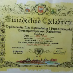 Skan świadectwa czeladniczego Ogólnopolskiej Izby Rzemieślniczej dla bioenergoterapeuty Agaty Wypiór, z herbami różnych rzemiosł po bokach i rysunkiem miasta na dole.