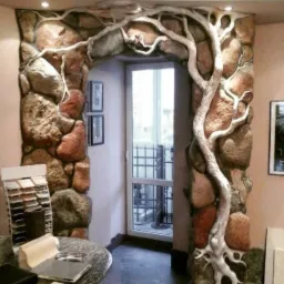 Wykończenie otworu drzwiowego imitacją kamienia i korzeni drzewa, z ekspozytorem próbek materiałów na pierwszym planie.