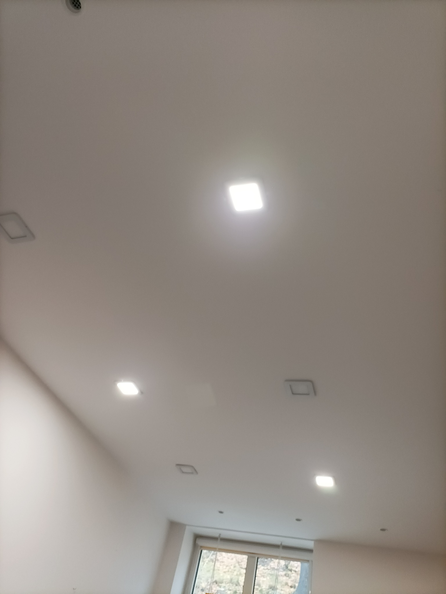 Biały sufit z równomiernie rozmieszczonymi kwadratowymi lampami LED, widok z dołu.