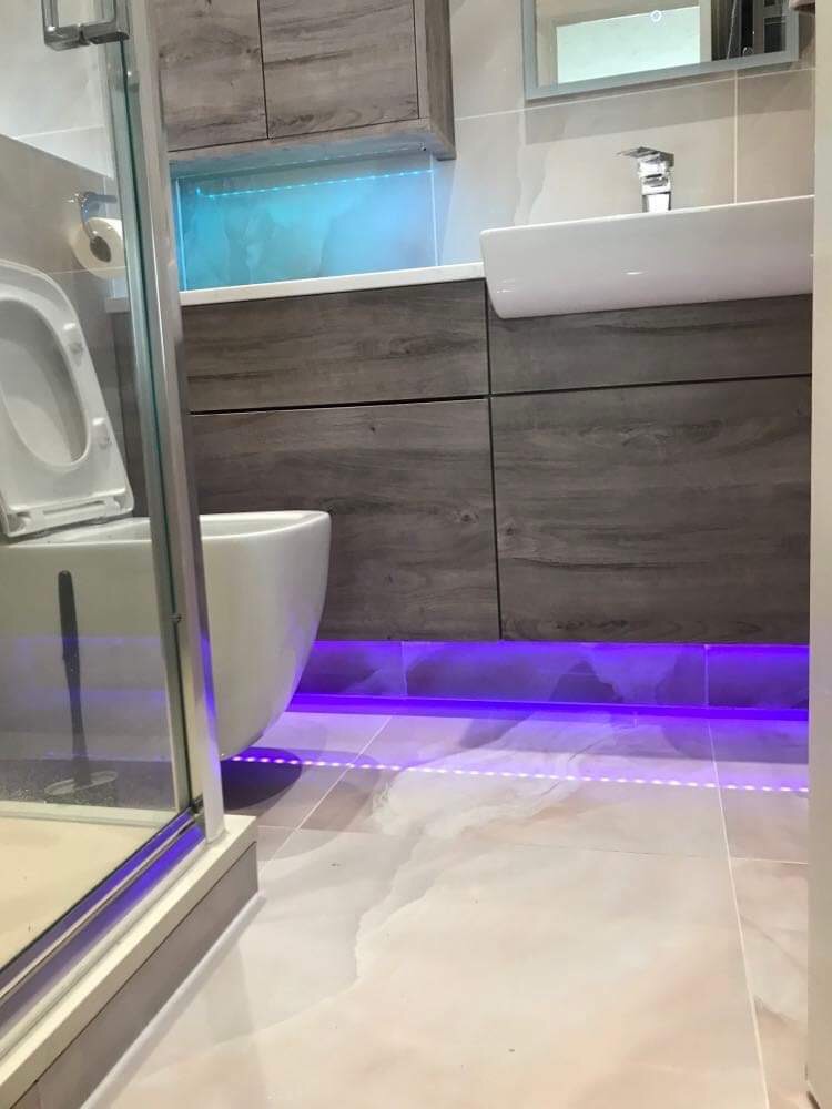 Nowoczesna łazienka w Krościenku nad Dunajcem z podświetleniem LED pod szafką umywalkową i toaletą, widok na kabinę prysznicową z boku i płytki podłogowe imitujące marmur.