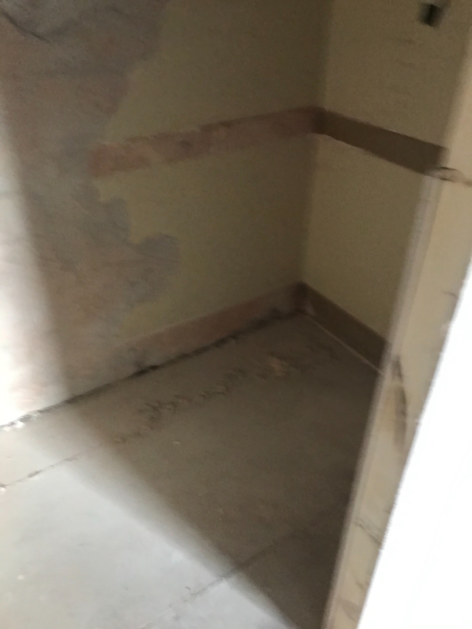 Niedokończone wnętrze pomieszczenia z surowymi ścianami, widoczne ślady po usuniętych listwach przypodłogowych i fragmenty starej farby, przygotowane do dalszych prac wykończeniowych.