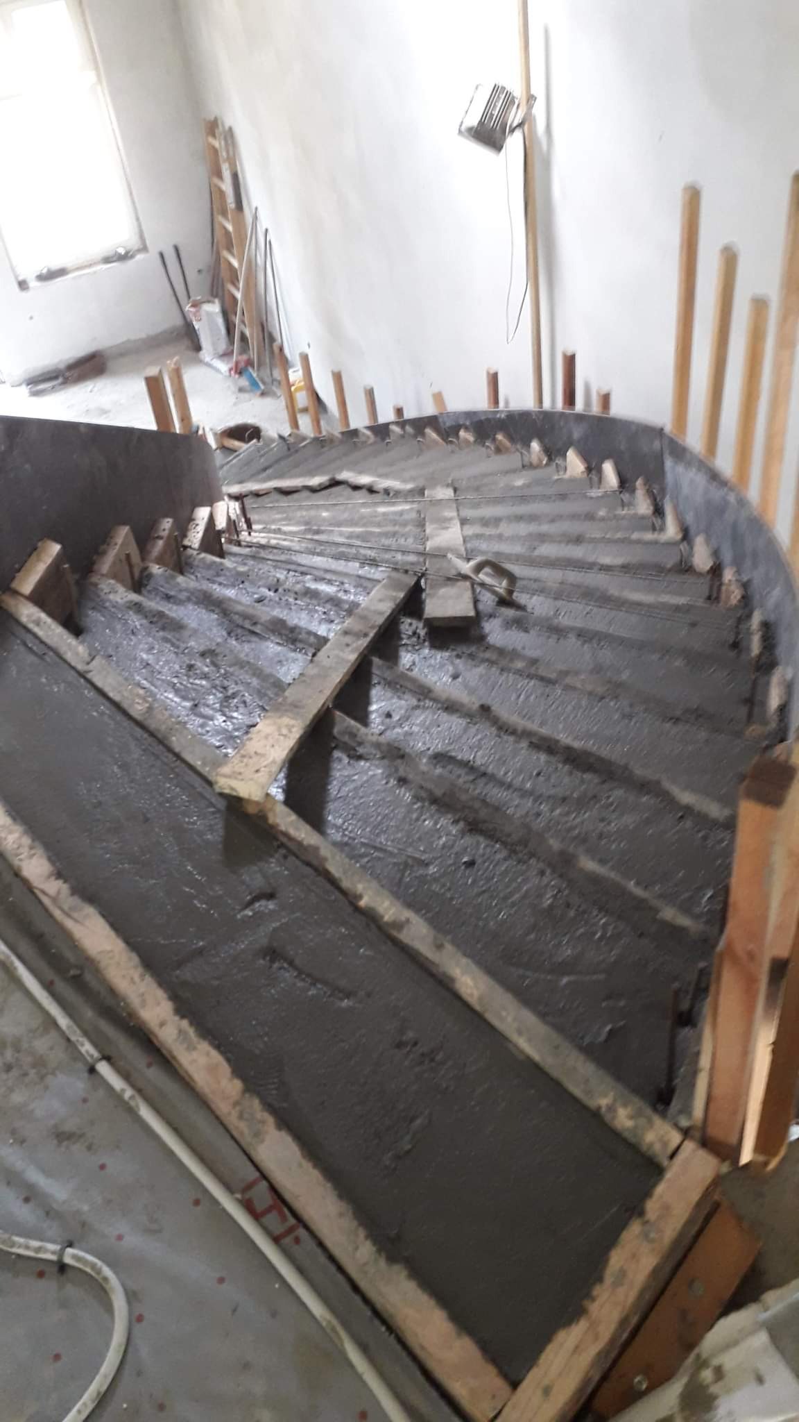 Wylewanie betonowych schodów spiralnych w szalunku z desek, widoczne podpory i tymczasowe wzmocnienia, wnętrze w trakcie budowy.