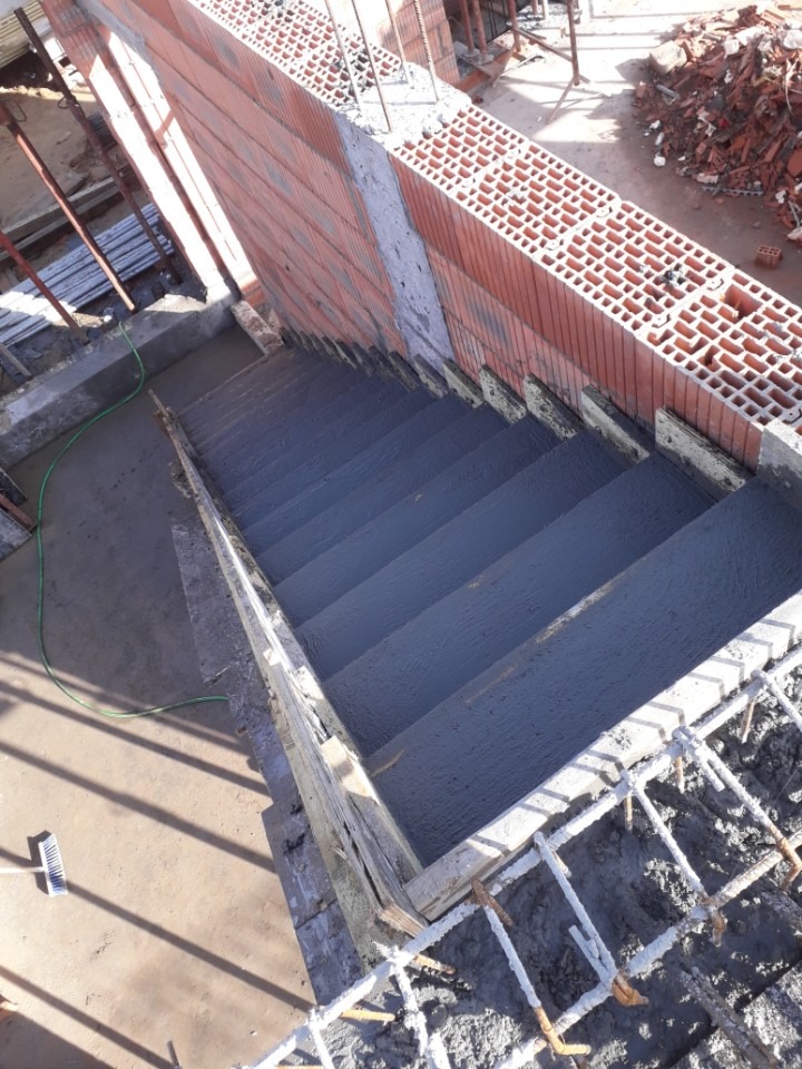 Wewnętrzne schody betonowe w trakcie wylewania, widoczne zbrojenia i pustaki ceramiczne na ścianie, szare stopnie, perspektywa z góry.