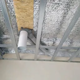 Instalacja kanałów wentylacyjnych pod sufitem podwieszanym z folią izolacyjną, widoczne rury i metalowa konstrukcja nośna.