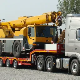 Ż&oacute;łty dźwig Liebherr przewożony na niskopodwoziowej, wieloosiowej platformie ciągniętej przez srebrną ciężar&oacute;wkę Volvo FH16 z dodatkowym oświetleniem na dachu kabiny.