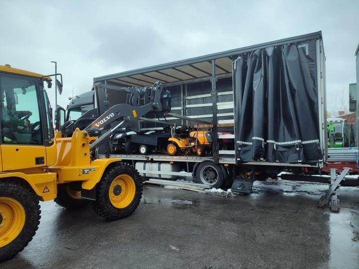 Żółta ładowarka Volvo obok otwartej naczepy ciężarówki, w której załadowane są małe traktorki ogrodowe.