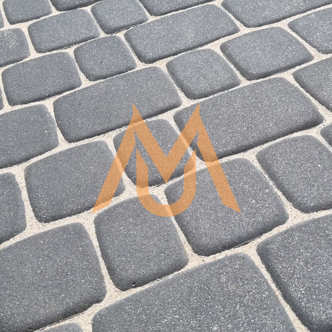 Szara kostka brukowa ułożona w regularny wzór, widok z bliska, z delikatnie zaokrąglonymi krawędziami i jasnymi fugami wypełnionymi piaskiem.