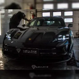 Czarny Porsche Taycan po detailingu, pracownik wyciera maskę mikrofibrą, widoczne logo firmy detailingowej Illegal Shine.