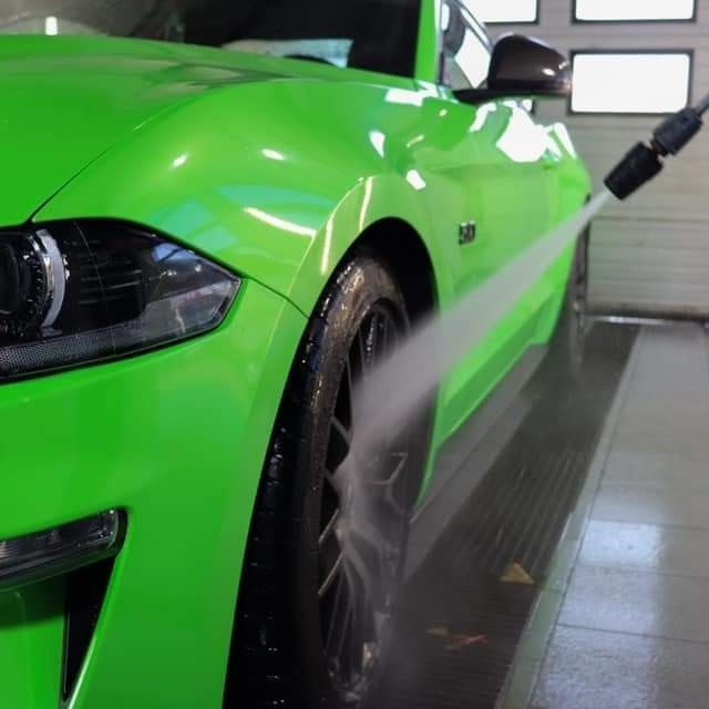 Jasnozielony samochód sportowy myty pod ciśnieniem w myjni, widok z boku na przednie koło i reflektor.
