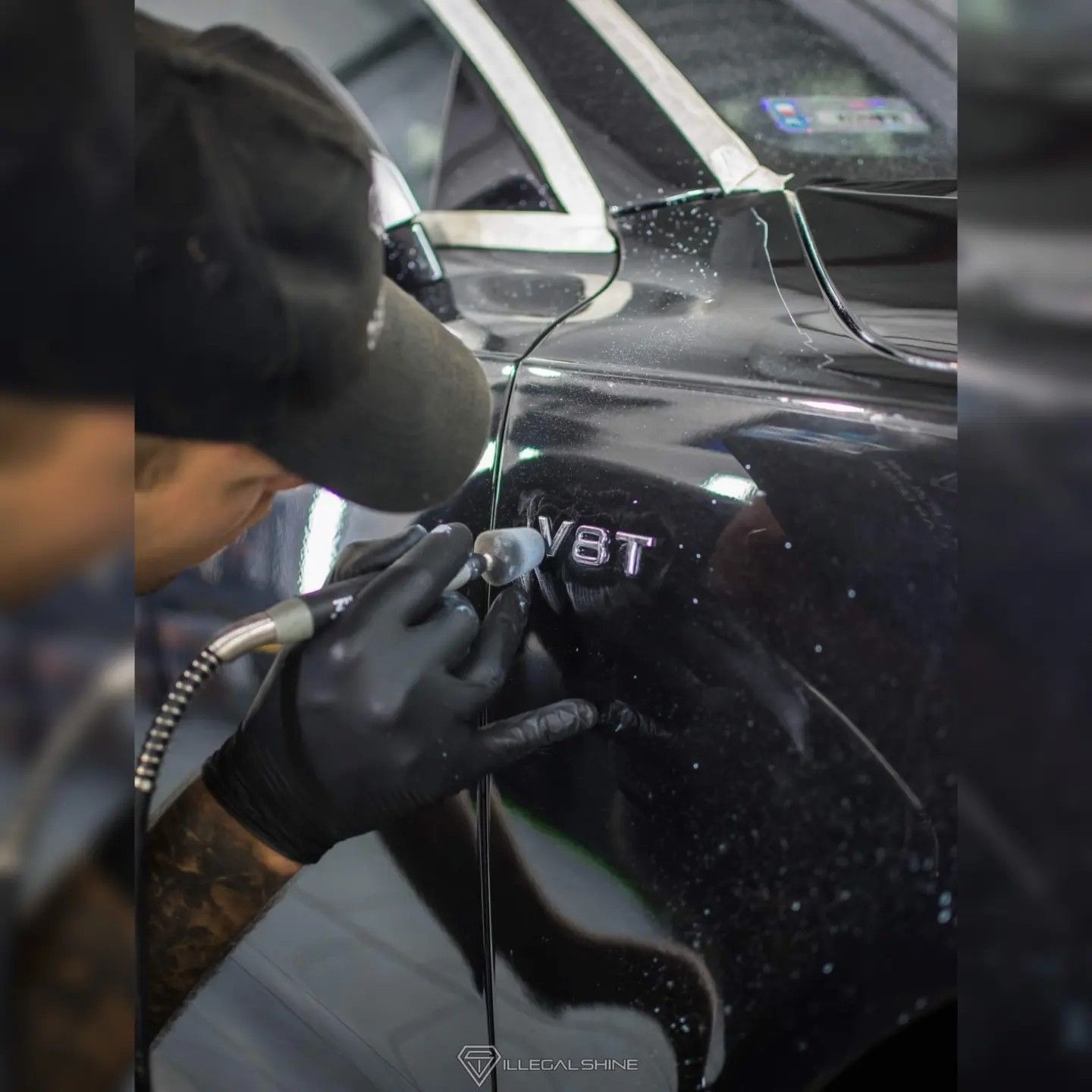 Detailer w czarnych rękawicach poleruje emblemat V8T na czarnym samochodzie, używając małej polerki rotacyjnej; widoczne ślady po polerowaniu.