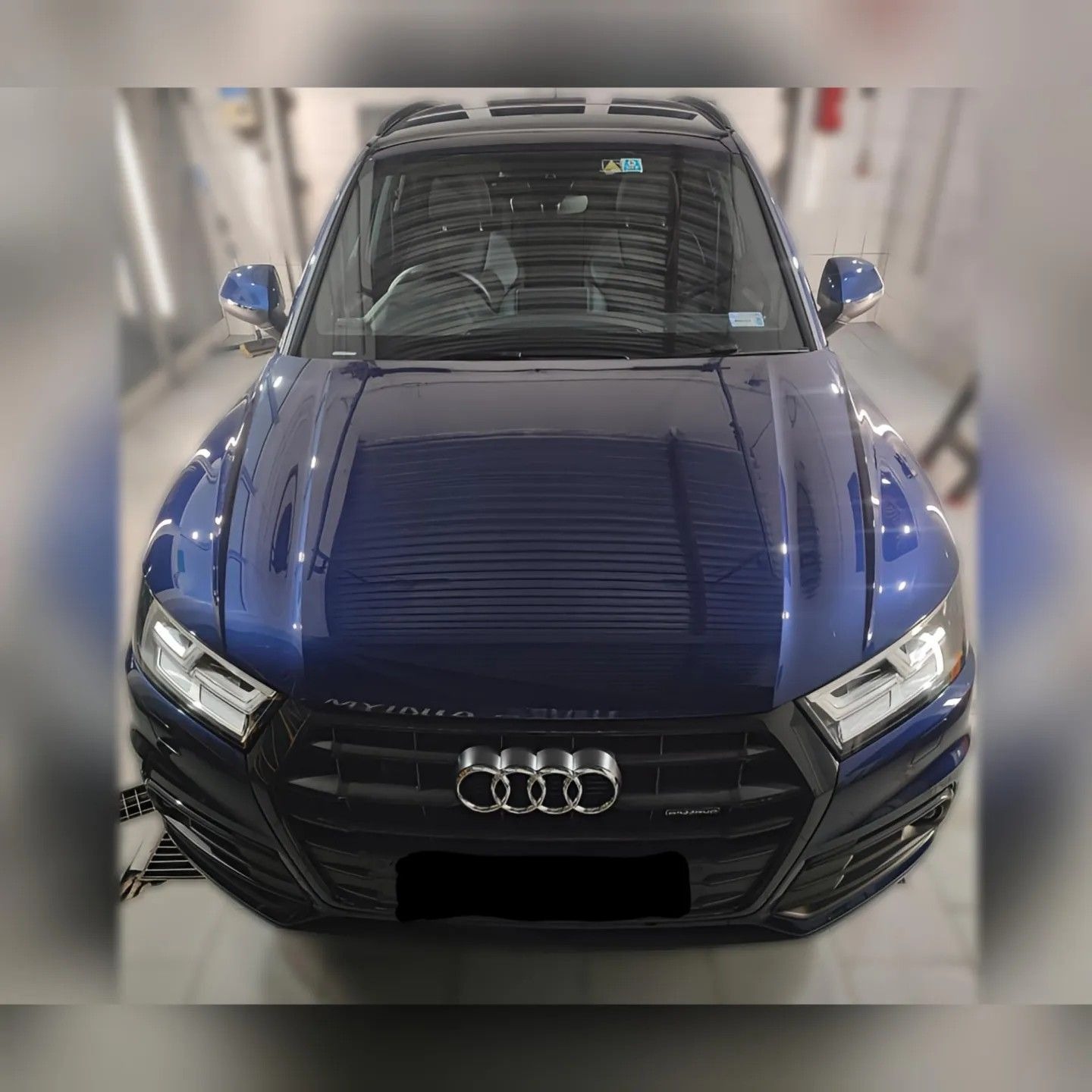 Błyszczący, granatowy samochód Audi Q5, widziany z przodu, zaparkowany w jasnym pomieszczeniu z metalowymi elementami, prawdopodobnie myjni.