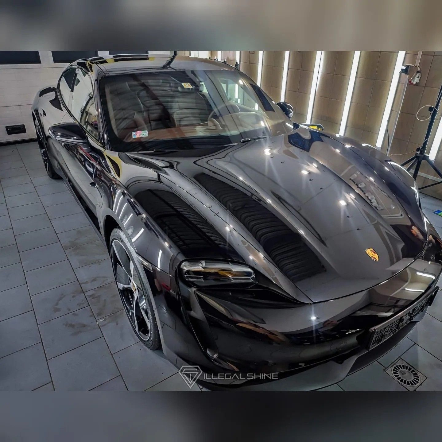 Błyszczący czarny Porsche Taycan po zabiegach pielęgnacyjnych, widoczne odbicia światła na karoserii, wnętrze w odcieniach beżu, logo firmy detailingowej w rogu zdjęcia.