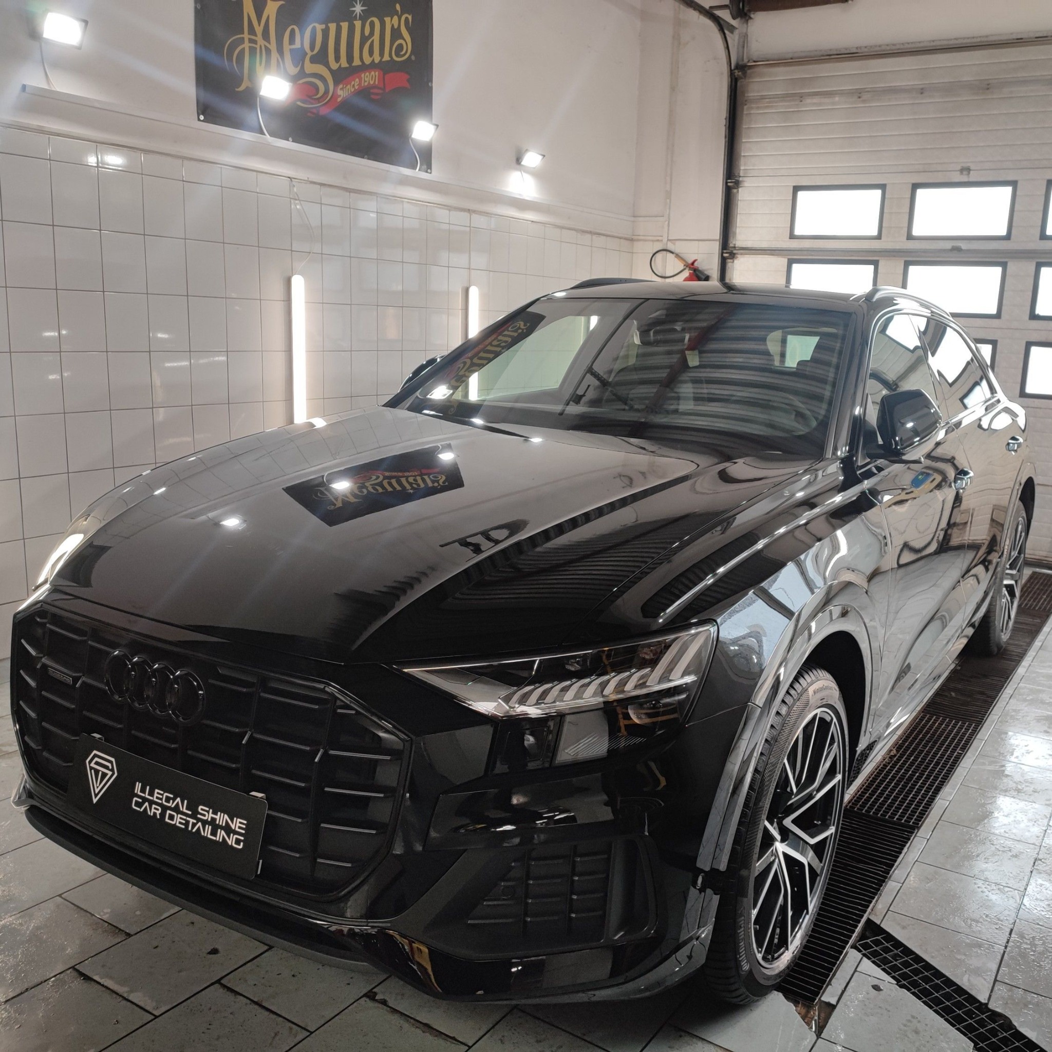 Błyszczący czarny Audi Q8 po detailingu w myjni, widoczny znak firmy 'Illegal Shine Car Detailing' na przednim zderzaku.