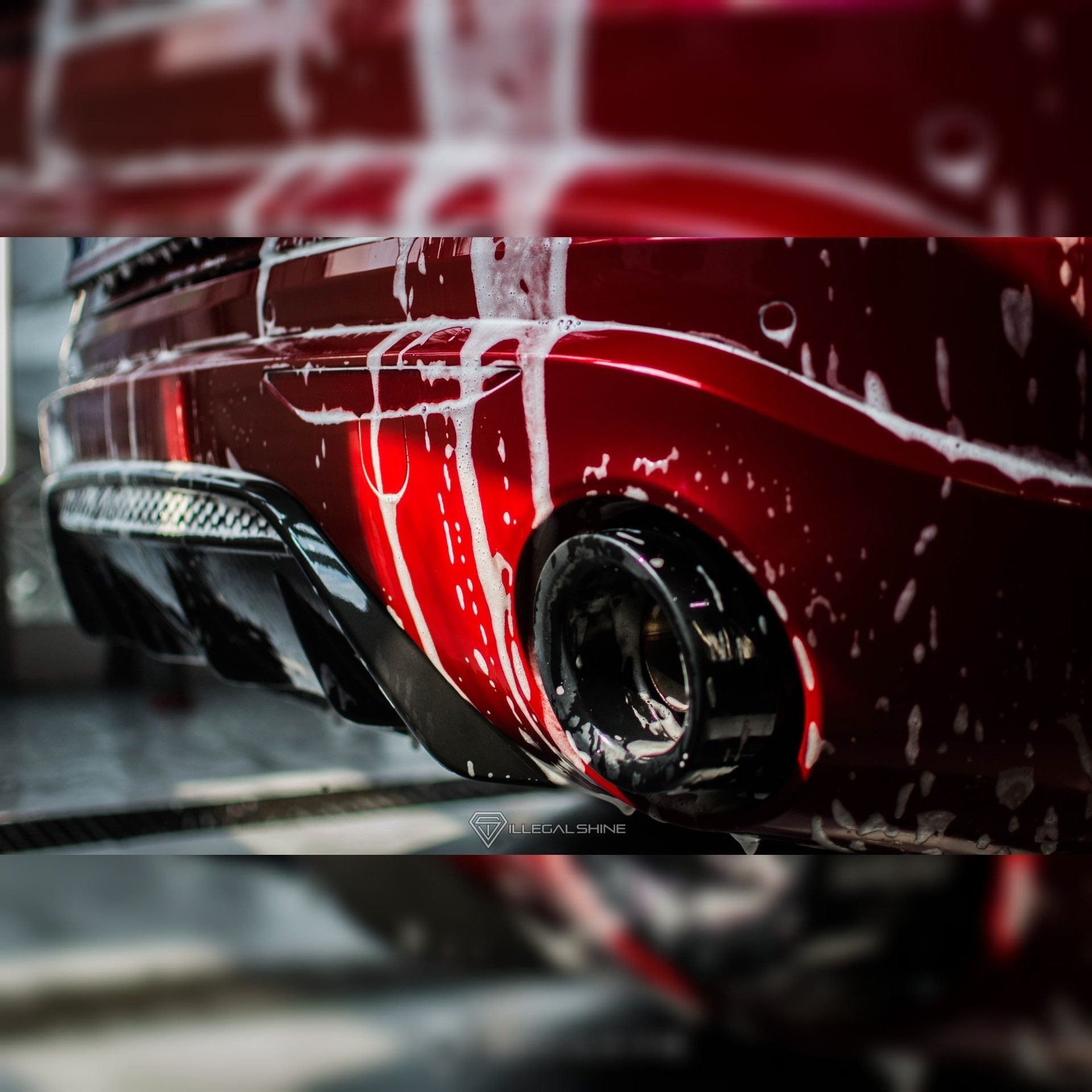 Czerwony samochód z widocznym tylnym zderzakiem pokryty spływającą pianą podczas mycia, zbliżenie na dyfuzor i końcówkę wydechu.