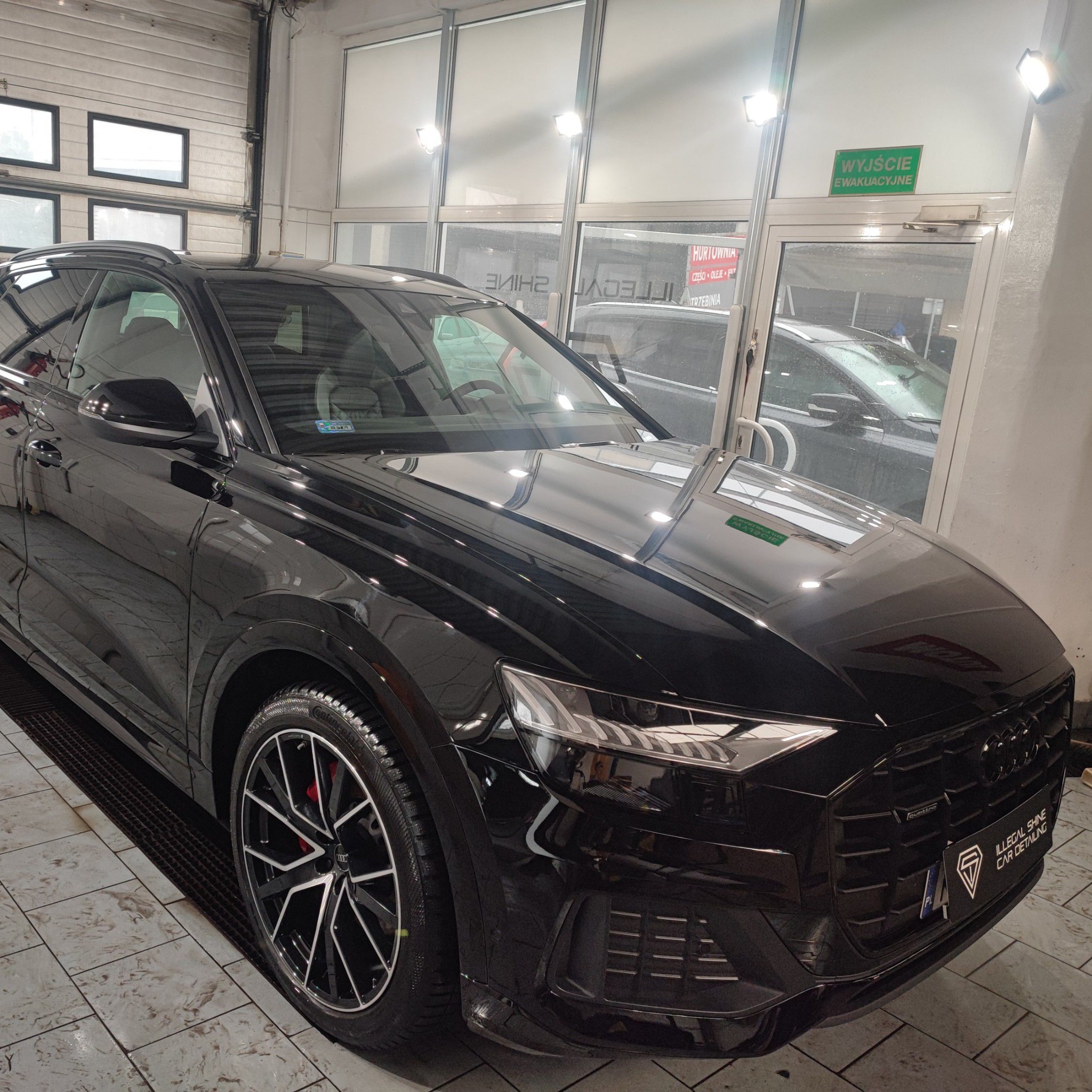 Błyszczący czarny SUV Audi Q8 po umyciu w myjni, widoczne odbicia w lakierze, felgi z czerwonymi zaciskami hamulcowymi, logo detailingu na przednim zderzaku.