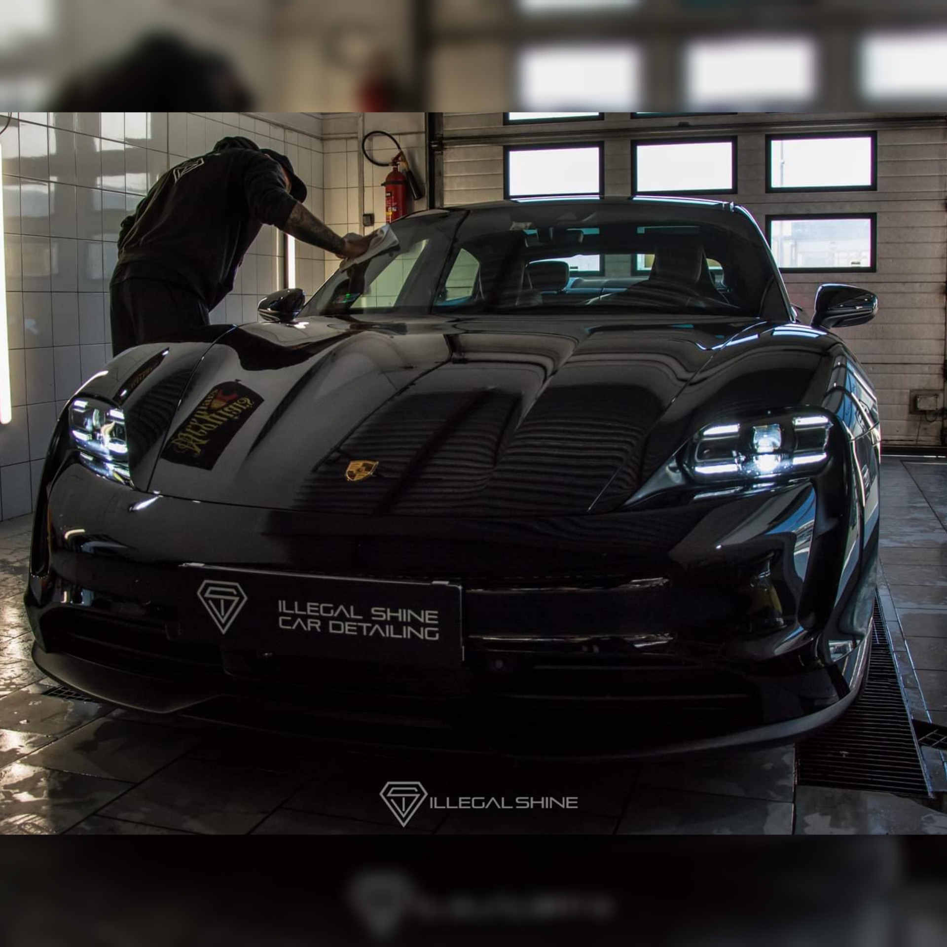 Czarny Porsche Taycan po detailingu, pracownik wyciera maskę mikrofibrą, widoczne logo firmy detailingowej Illegal Shine.