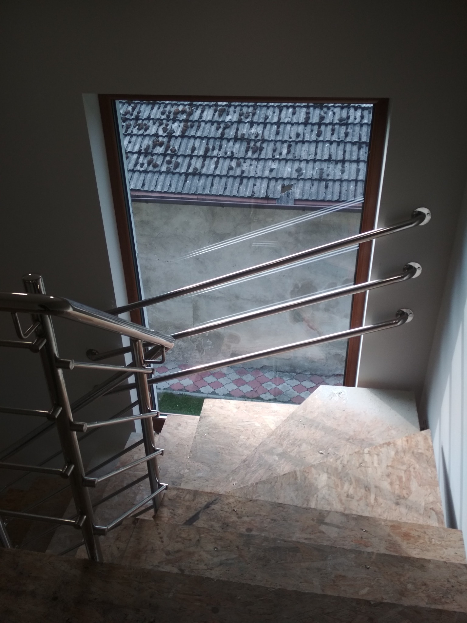 Widok z góry na schody wewnętrzne z okładziną imitującą kamień i stalową balustradą z trzema poziomymi prętami, widoczne okno dachowe z widokiem na dach pokryty dachówką.