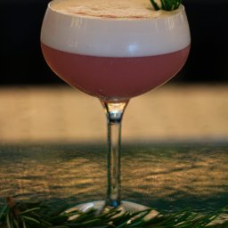 Barmates - Elegancki kieliszek z różowym koktajlem zwieńczonym pianką, udekorowany gałązką rozmarynu, leżącą również u podstawy kieliszka na teksturowanym blacie.