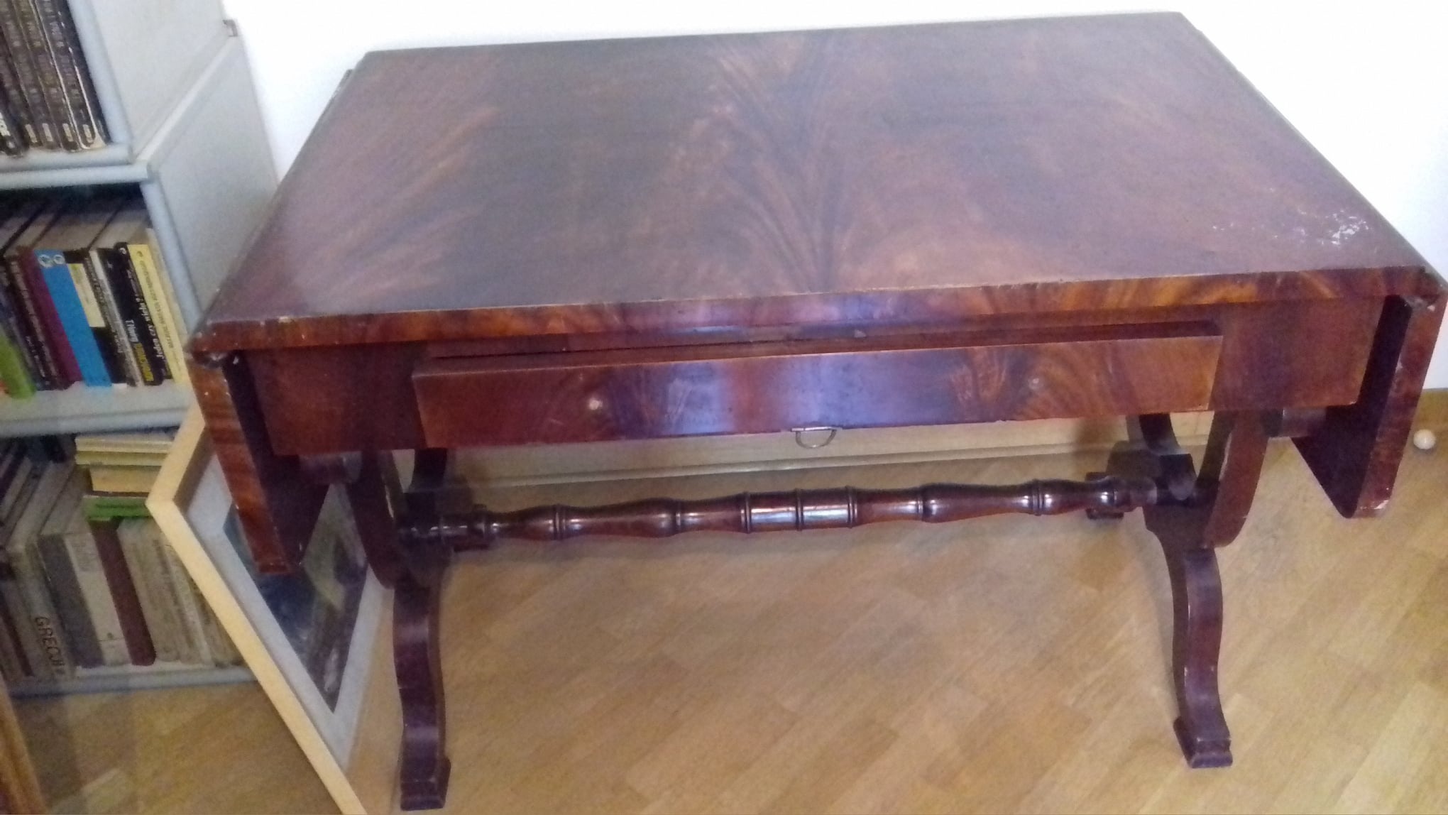 Antyczny, mahoniowy stół z szufladą i rozkładanym blatem, widoczne ślady użytkowania i odnowiona powierzchnia blatu.