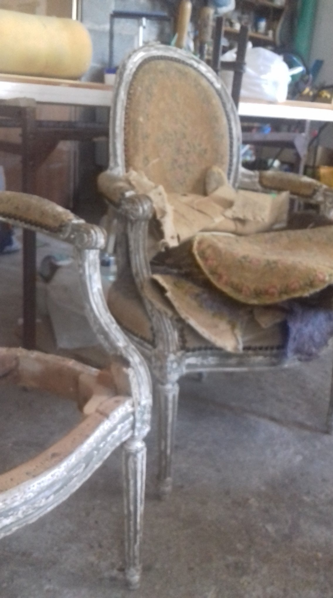 Antyczne krzesło z jasną ramą w trakcie renowacji, z częściowo zdjętą tapicerką i widocznymi warstwami materiałów.