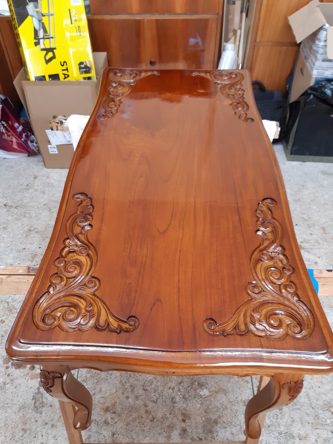 Błyszczący, odrestaurowany stół z ciemnego drewna z rzeźbionymi zdobieniami w narożnikach, po renowacji.