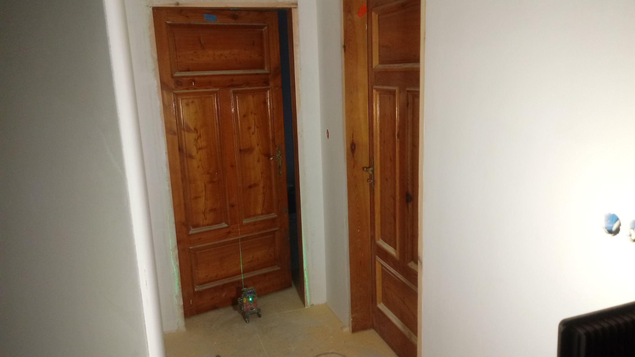 Dwa drewniane, fornirowane drzwi w trakcie montażu, widoczny laser krzyżowy ustawiający pion w ościeżnicy, surowa ściana po remoncie.