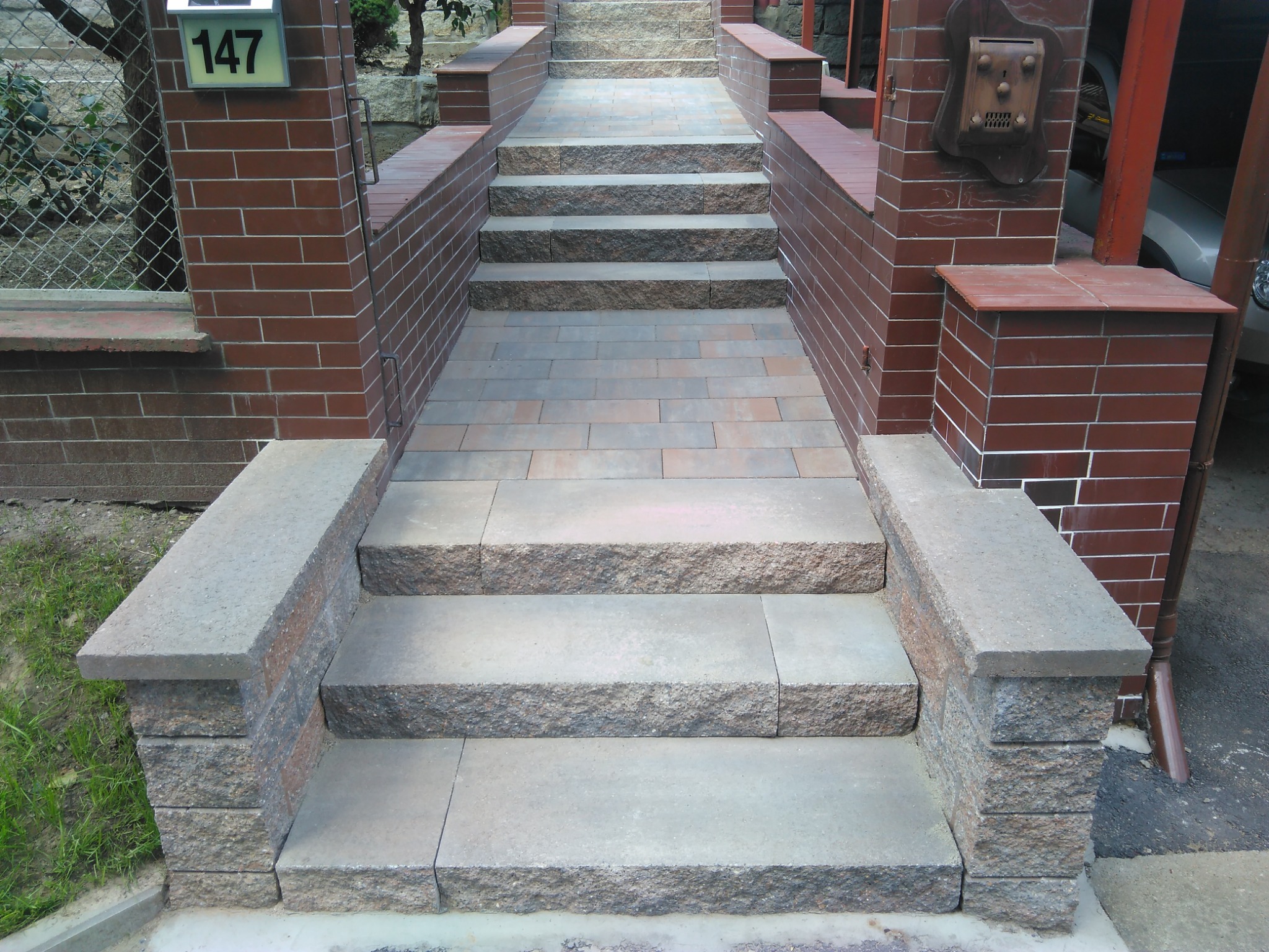 Schody wejściowe z kostki brukowej prowadzące do domu, z numerem 147 na murze i ozdobną skrzynką na listy.