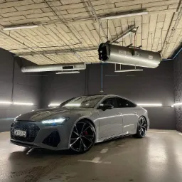 Szary samochód Audi RS7 po myciu w profesjonalnej myjni, widoczne krople wody na podłodze i oświetlenie sufitowe