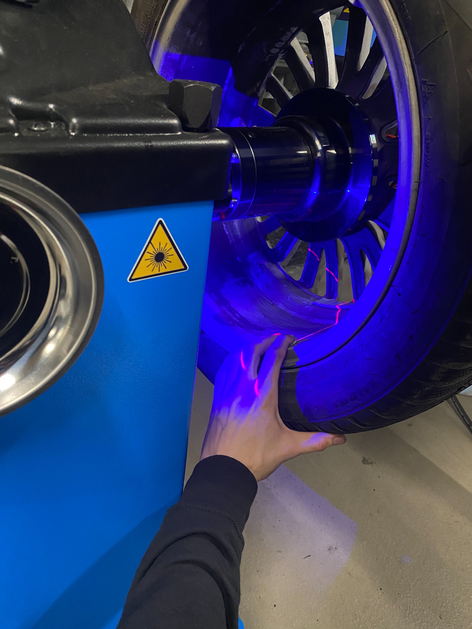 Czyszczenie felgi aluminiowej w myjni z użyciem lasera, felga oświetlona niebieskim światłem, widoczna dłoń pracownika.